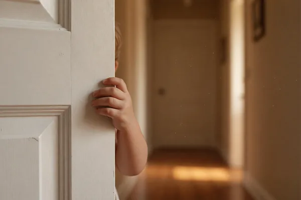A young child's hand gripping a doorframe in a hallway, hesitant to leave for the other parent's home
