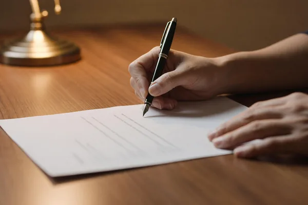 A pair of hands signing an agreement with a fountain pen at a desk