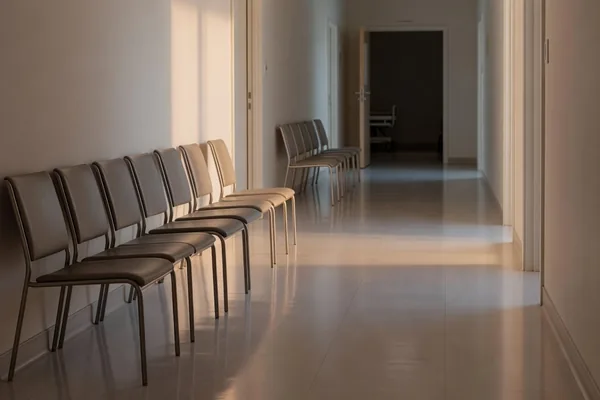 A quiet hospital corridor lined with empty visitor chairs outside patient rooms, where hospital visitation rights matter
