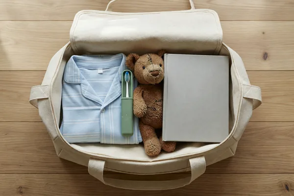 A child's overnight duffel packed with pajamas, a toothbrush, a stuffed bear and a book before a handoff
